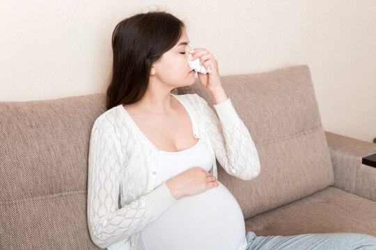 Sick pregnant woman blowing nose into tissue at home Healthy millennial healthcare concept
