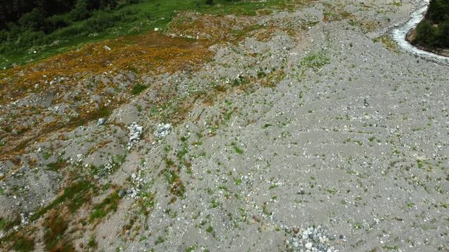 Dramatic aerial photography flying over the remnants of a devastating landslide in Georgia's remote Shovi Racha mountain valley, revealing a wide path of rocks and debris among lush green coniferous f