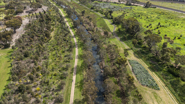 Aerial view of narrow waterway of Laverton Creek surrounded by native bushland, walking trails, and open parkland in Altona Meadows, Melbourne Australia. Riparian corridor, environmental conservation