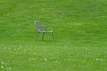 A single grey mesh outdoor armchair stands alone in the middle of a lush green lawn dotted with tiny white flowers. © Jakob