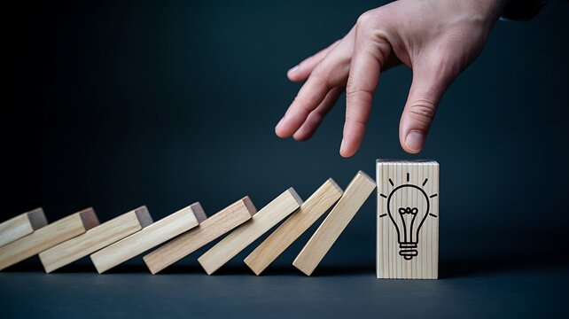 Business concept showing a hand protecting a standing light bulb from falling dominoes as a symbol of innovation