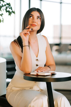 Thoughtful young woman sitting at a table with a pen and notebook in a bright modern office setting