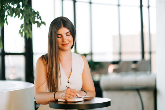 Professional woman writing notes in a notebook at a modern table inside a bright cafe during the day
