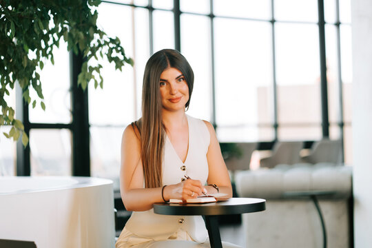 Professional woman writing in a notebook while sitting at a table in a bright office during daytime