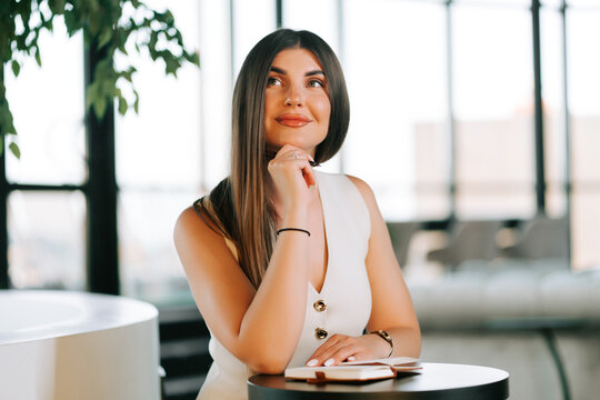 Professional woman with long hair sitting at a table while brainstorming during the daylight hours