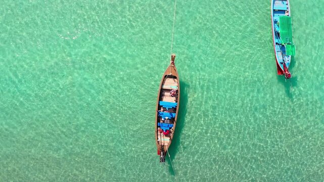 Aerial top down view of two traditional long tail boats floating over transparent turquoise water, sunlight on ocean ripples and sandy seabed, tropical island travel and serene escape to Thailand