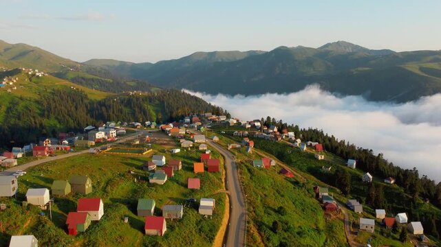 Aerial view of the stunning mountain village of Gomis mta in Georgia with bright houses nestled on a green slope above a sea of clouds at dawn, showcasing a calm and picturesque landscape