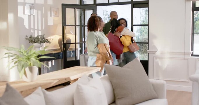 Friends entering at home's front entry, woman in green pointing, hugging, greeting