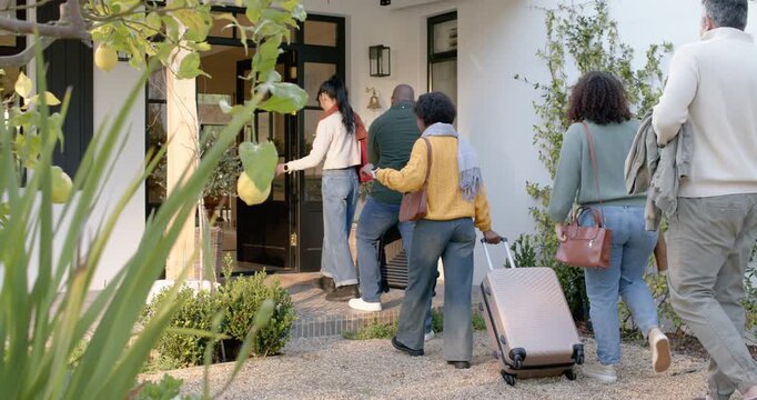 Diverse five friends arriving at porch, pulling rolling suitcases and entering house
