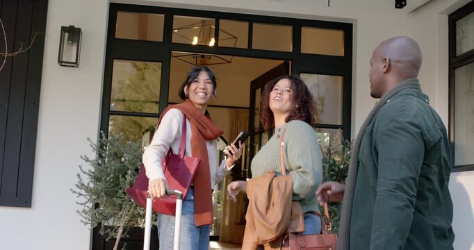 African American friends arriving, checking map on smartphone, pulling suitcases and entering home