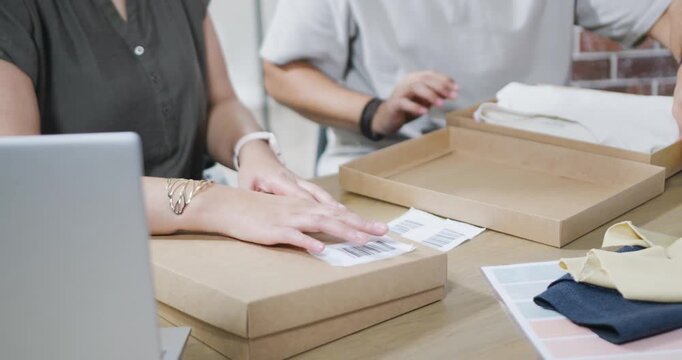 Printed shipping label is appearing on table while pair are labeling and packing boxes for shipping