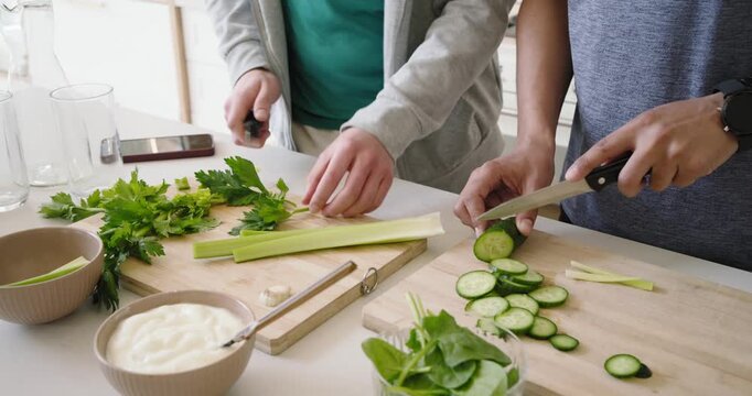 Right person is starting by slicing cucumber while left person is chopping celery for salad prep