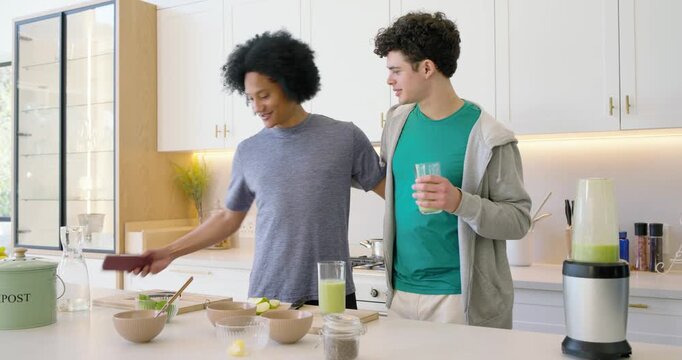 Two African American men posing for selfies with phone at kitchen island after blending green drink