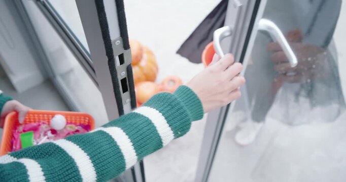 African American child knocking at glass door, resident giving orange basket, filling pumpkin pail