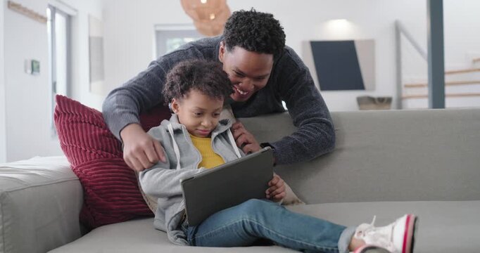 African American family reacting to child tapping tablet, parents leaning over sofa guiding hands
