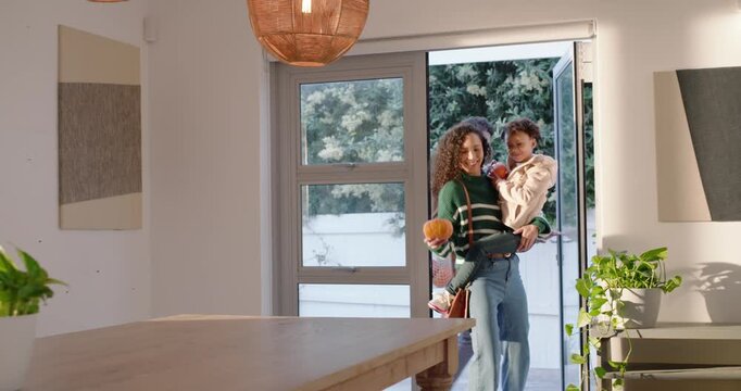 African American family entering patio door carrying pumpkins, placing gourds on table for display