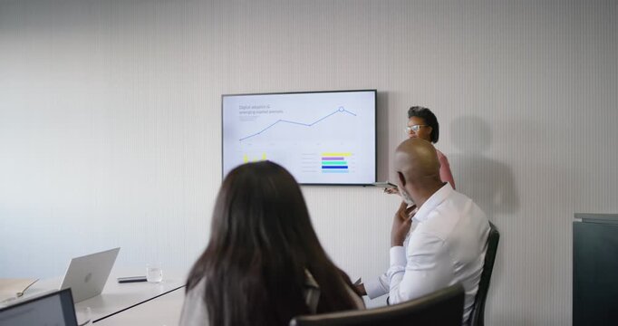 Diverse team noticing slide change woman pointing at screen with tablet showing charts in office