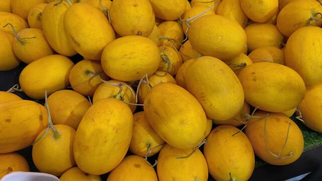 Fresh canary melons are piled neatly on a table for display. These bright yellow fruits are ready for sale at a local market.