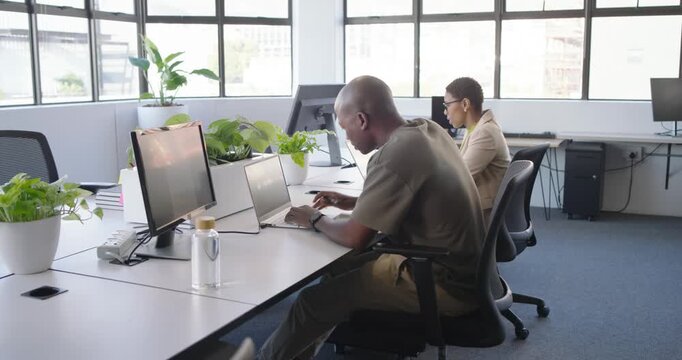African colleagues working at desk after man glancing, leaning and pointing with pen at laptop data