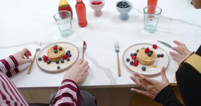 Two diners are reaching for cutlery at counter, prompted by matching pancake plates with berries