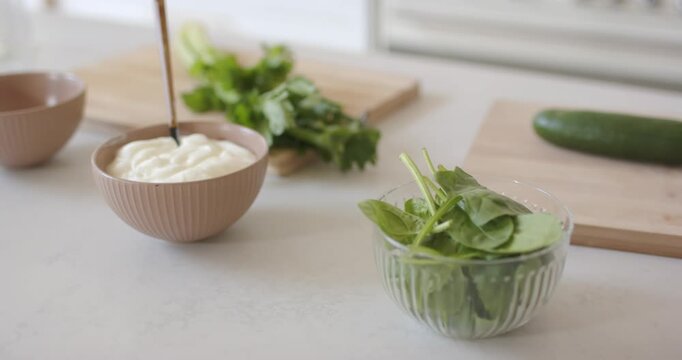 Off-screen hand is placing ribbed bowl of dressing on counter then is reaching celery for salad