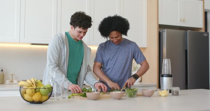 African American men in kitchen cutting greens on boards reaching for apple passing and making meal