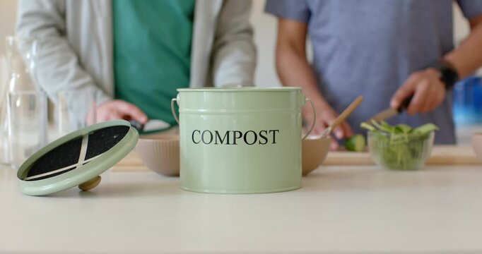 Knife is slicing salad greens, hands are dropping scraps into pale green compost pail on counter