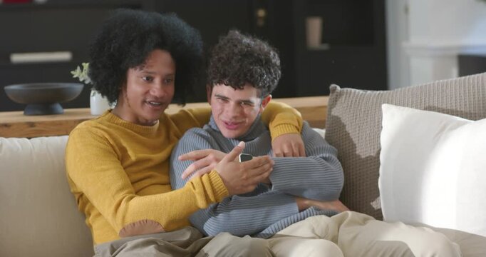 African American dad and teen son sitting on sofa, dad noticing smartwatch, son leaning and smiling