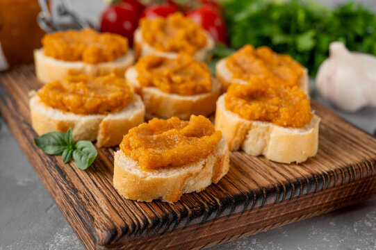 Zucchini caviar on baguette slices, served as a homemade appetizer on a rustic board with fresh herbs and vegetables. Healthy food.