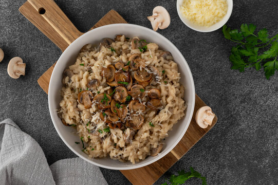 A creamy mushroom risotto topped with parmesan and herbs, served in a white bowl on a dark background. Top view, copy space.