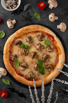 Halloween mushroom pizza with basil, cheese and spooky skeleton decoration on a dark background, creative food concept for seasonal menus. Funny food idea. Top view.