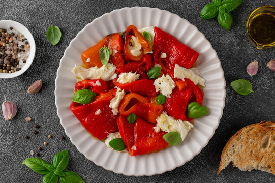 Salad with roasted red peppers and mozzarella in olive oil and garlic on a plate on dark background. Mediterranean appetizer served with bread. Top view.