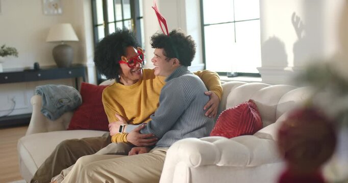 African American male friends sitting on white couch at home, red antlers sparking laughter
