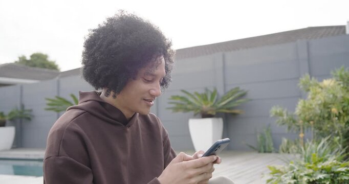African American man in brown hoodie tapping smartphone, scrolling, finishing reply on pool deck