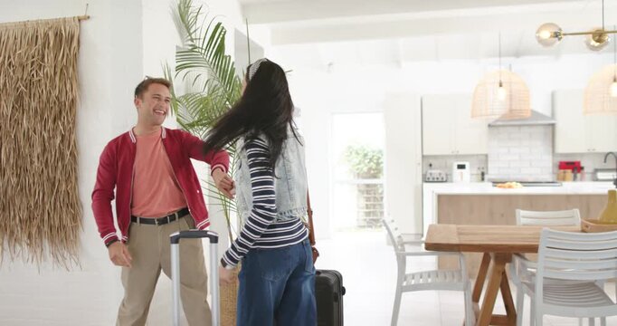 Couple arriving at open-plan home with two suitcases, greeting, twirling, hugging, reuniting