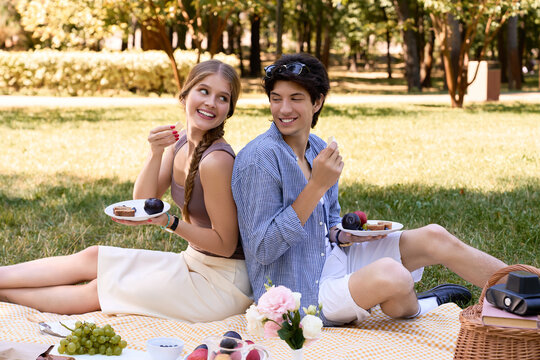 A happy couple shares delicious treats while seated on a picnic blanket in a lush park