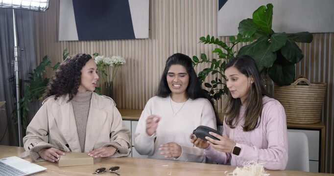 Diverse women, left woman opening box on set, passing zip case, unzipping sunglasses, reviewing