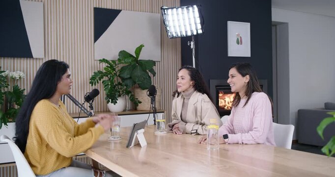 Diverse women podcasting at wooden table with mics, host in yellow sweater speaking