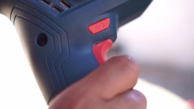 Person pulling drill trigger close up shot, activating power tool, construction equipment and DIY project concept.