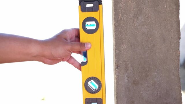 Person checking wall alignment with bubble level close up, construction work, measurement and building concept.