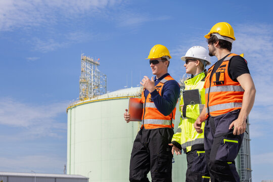 Multiethnic industrial engineers team walking and talking at lng plant facility, diverse project managers in safety gear discussing work outdoors at gas storage facility