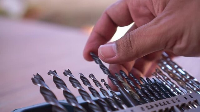 Hand returning steel drill bit to storage container, close up shot, hardware tool organization, workshop equipment footage.