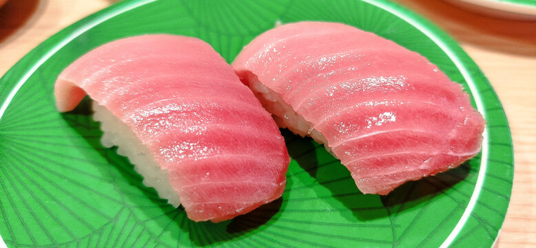 A melt-in-your-mouth piece of fatty chutoro tuna sushi, featuring beautifully marbled raw fish draped over vinegared rice and presented on a bright green ceramic dish.