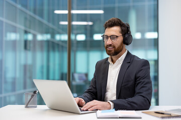 Portrait of a young businessman in a suit and headset working intently in the office at a laptop