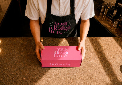 Barista Holding Packaging Box and Apron Mockup on Coffee Shop Counter