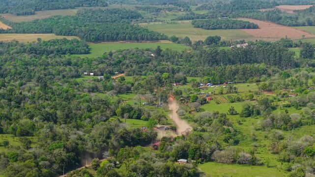 Drone shot of a rally car speeding on a dusty rural dirt road, followed by a helicopter, set amidst lush green countryside near Nueva Alborada.