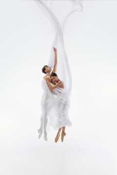 Suspended ballet duo floats vertically beneath delicate white textile. Concept of weightlessness, freedom, synchronized effort, imagination, and transcending boundaries.