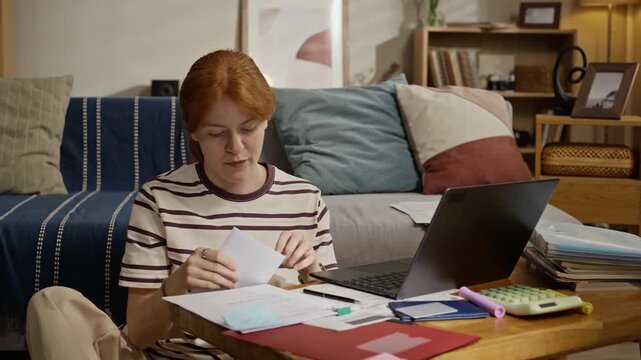 Caucasian young adult woman opening envelope and looking stressed while reviewing utility bills as camera zooms in. Clip suitable for banking, budgeting apps, or financial stress campaigns