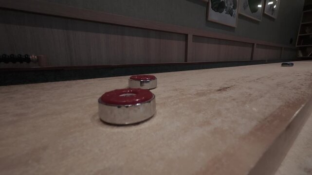 Slow motion blue shuffleboard puck knocking two red pucks off