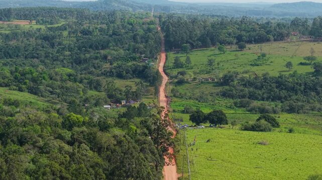 Drone video captures a winding dirt rally track for the WRC 2026 in Nueva Alborada, Paraguay, cutting through lush green countryside under bright daylight, showcasing panoramic rural scenery.